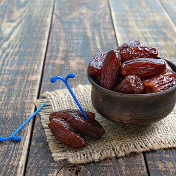 Dried dates fruit in ceramic bowl on old wooden table. Highly valuable food product.