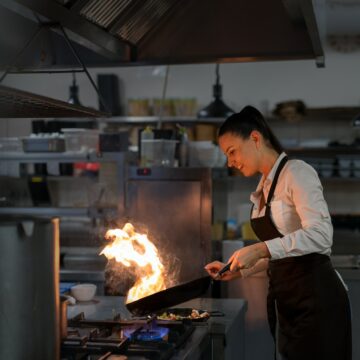 Professional chef preparing meal, flambing indoors in restaurant kitchen
